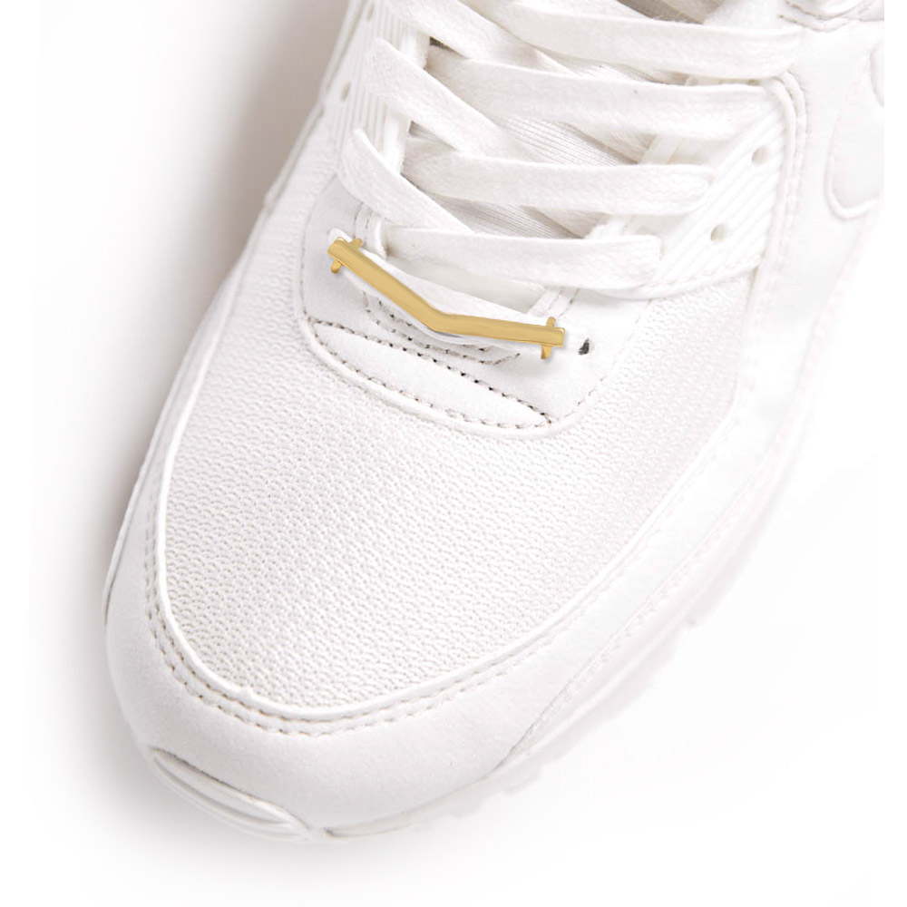 Close-up of a stylish V-shape gold-plated shoe charm attached to the laces of a white sneaker, showcasing a unique fashion accessory.