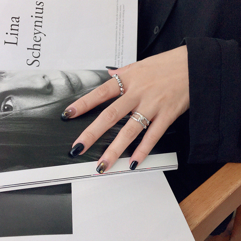 A woman's hand with black nail polish wearing a set of five 925 sterling silver minimalist rings, resting elegantly on a magazine.