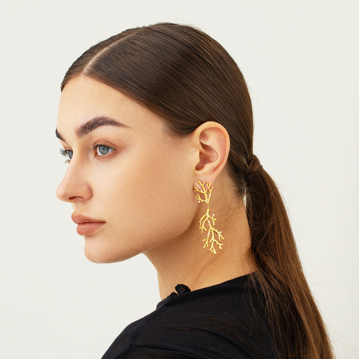 A woman modeling the elegant stainless steel gold-plated pearl and coral branch drop earrings, showcasing their sophisticated design.