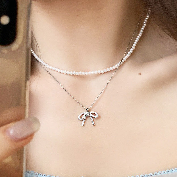 A model wearing an elegant 925 sterling silver bow-knot necklace with sparkling zircon stones, layered with a pearl choker. A wholesale jewelry piece from JR Fashion Accessories.