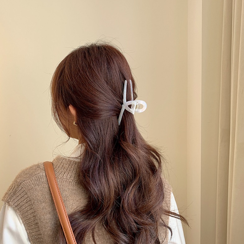 A woman with blonde hair wearing a beige outfit, showcasing a large white acetate hair claw clip in a stylish low ponytail.