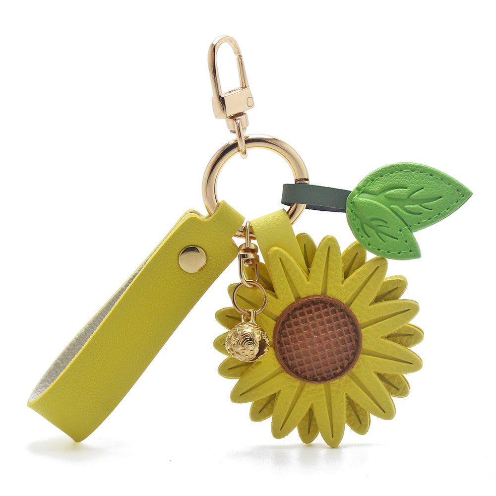 A vibrant yellow PU leather sunflower keychain with a gold bell charm and leaf accent, designed as a lucky charm for exams and graduation gifts.