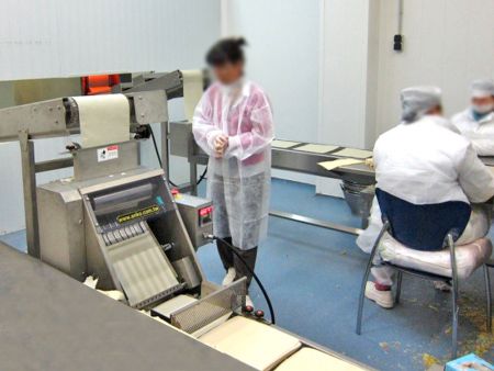 Employees working beside the conveyor belt ready to hand wrap Spring Rolls