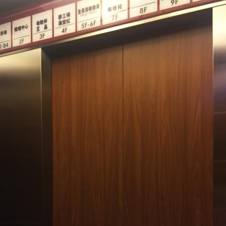 Záběr zblízka na vchod do výtahu s použitím ořechového dekoru z PVC laminovaného kovu na zdobení stěn výtahu