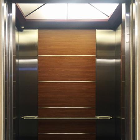 Зближений знімок передніх дверей ліфта, де для прикраси стін ліфта використовуються металеві сталеві плитки з ПВХ під дубову фактуру