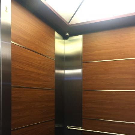 Närbild av vänster sida av en hiss med användning av valnötsfärgad PVC-laminerad metallplåt för att dekorera hissväggarna