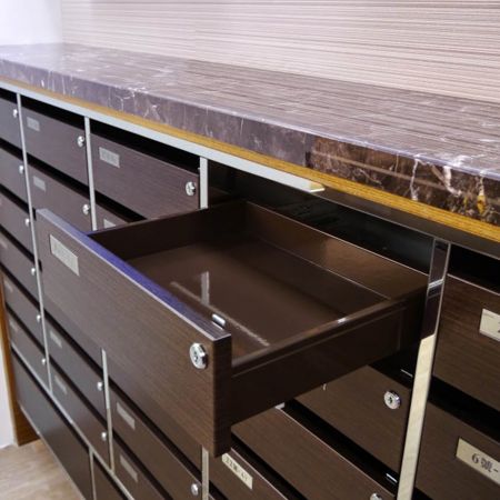 Bir binadaki lüks bir posta kutusunun yakından çekilmiş sağ tarafı, Kassod tahıl PVC laminasyonlu metal levhalarla dekore edilmiştir. Üst sıradaki çekmecelerden biri açılmış durumda.