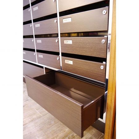 Bir binadaki lüks bir posta kutusunun yakından çekilmiş sağ tarafı, Kassod tahıl PVC laminasyonlu metal levhalarla dekore edilmiştir. Alt sıradaki çekmecelerden biri açılmış durumda.