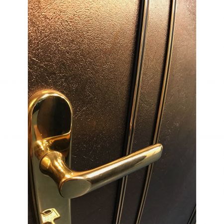 Egy klasszikus stílusú biztonsági ajtó bal oldalának közelképe, beleértve az utánzat réz kilincset és a Réz Fríz laminált fémlemezekkel díszített háromdimenziós textúrákkal teli felületeket