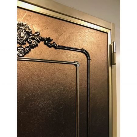 Visão de perto do lado direito de uma porta de segurança de estilo clássico, incluindo uma moldura de porta com design de imitação de cobre e superfícies cheias de texturas tridimensionais decoradas com placas de metal laminado com textura Brass Frieze