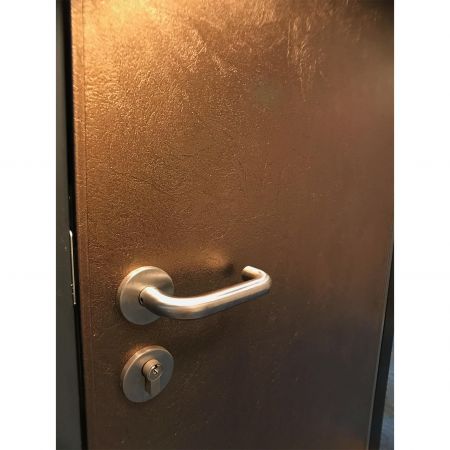 Pandangan dekat sisi kanan pintu keamanan gaya modern, termasuk pegangan pintu stainless steel dan permukaan yang penuh dengan tekstur tiga dimensi yang dihiasi dengan pelat logam laminasi Brass Frieze