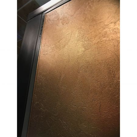 Közeli kép egy modern stílusú biztonsági ajtó bal oldaláról, melynek felületét Brass Frieze laminált fémlemezek díszítik