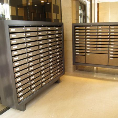 Два кластерні поштові скриньки, розташовані окремо від стіни, прикрашені ламінованими металевими пластинами з латунною фризою