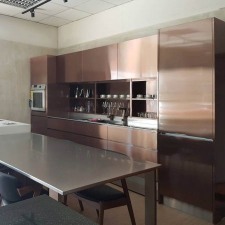 The bright modern style kitchen includes stainless steel countertops and an entire wall of kitchen cabinets made of Rose Gold anti-fingerprint stainless steel plates