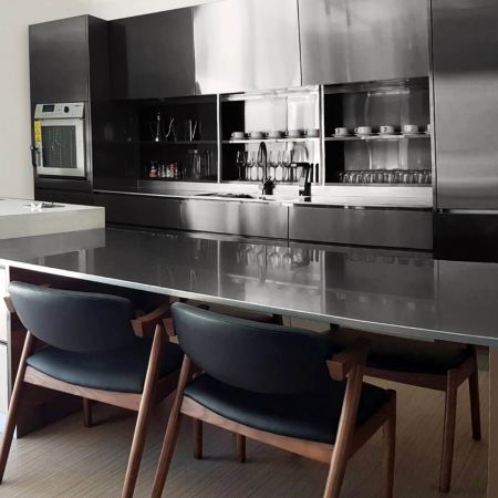 The bright modern style kitchen includes stainless steel countertops and an entire wall of kitchen cabinets made of trendy black anti-fingerprint stainless steel plates