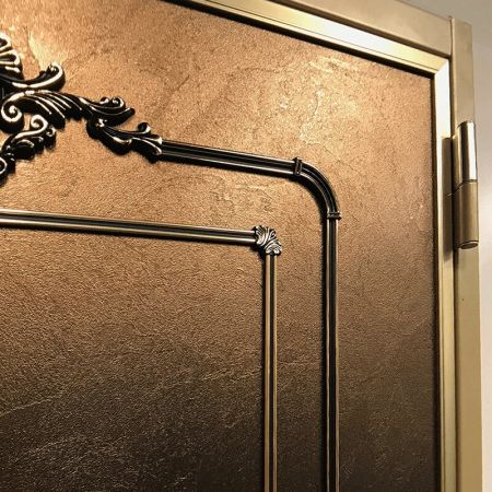 Класична броньована двері з поверхнею, прикрашеною ламінованими металевими плитами з латунним фризом