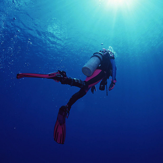 Un buceador con un traje de neopreno a medida, sumergido bajo el agua, mostrando ropa deportiva acuática para buceo y surf.