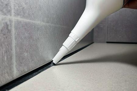 Applying mold-resistant silicon sealant on bathroom tiles.