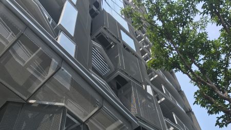 On the west side roof of the residential building, a metal curtain with intricate angles and shapes is designed to follow the direction of direct sunlight. At noon, under the scorching sun, the straight rays of sunlight refract through the wide mesh, gently passing through the surrounding space as a gentle breeze flows.