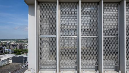 To add a touch of nature and soften the modern look of the building, greenery has been thoughtfully incorporated. What really sets this building apart is its top floor, which is enclosed by a large expanded metal mesh. This multi-functional mesh serves as both a sunscreen and a robust security barrier.