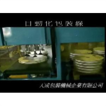 自動套袋收縮裝箱包裝系統 30-2 - 藍色包裝機械正在處理圓形金屬物件,左側有機械臂操作,右側堆疊著多個金屬圓盤。