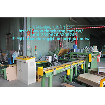 Long Floor Tile Packing Machine - A green and yellow industrial machine with a white control panel inside a factory, surrounded by stacked brown cardboard boxes. The company name and contact information are overlaid on the image.